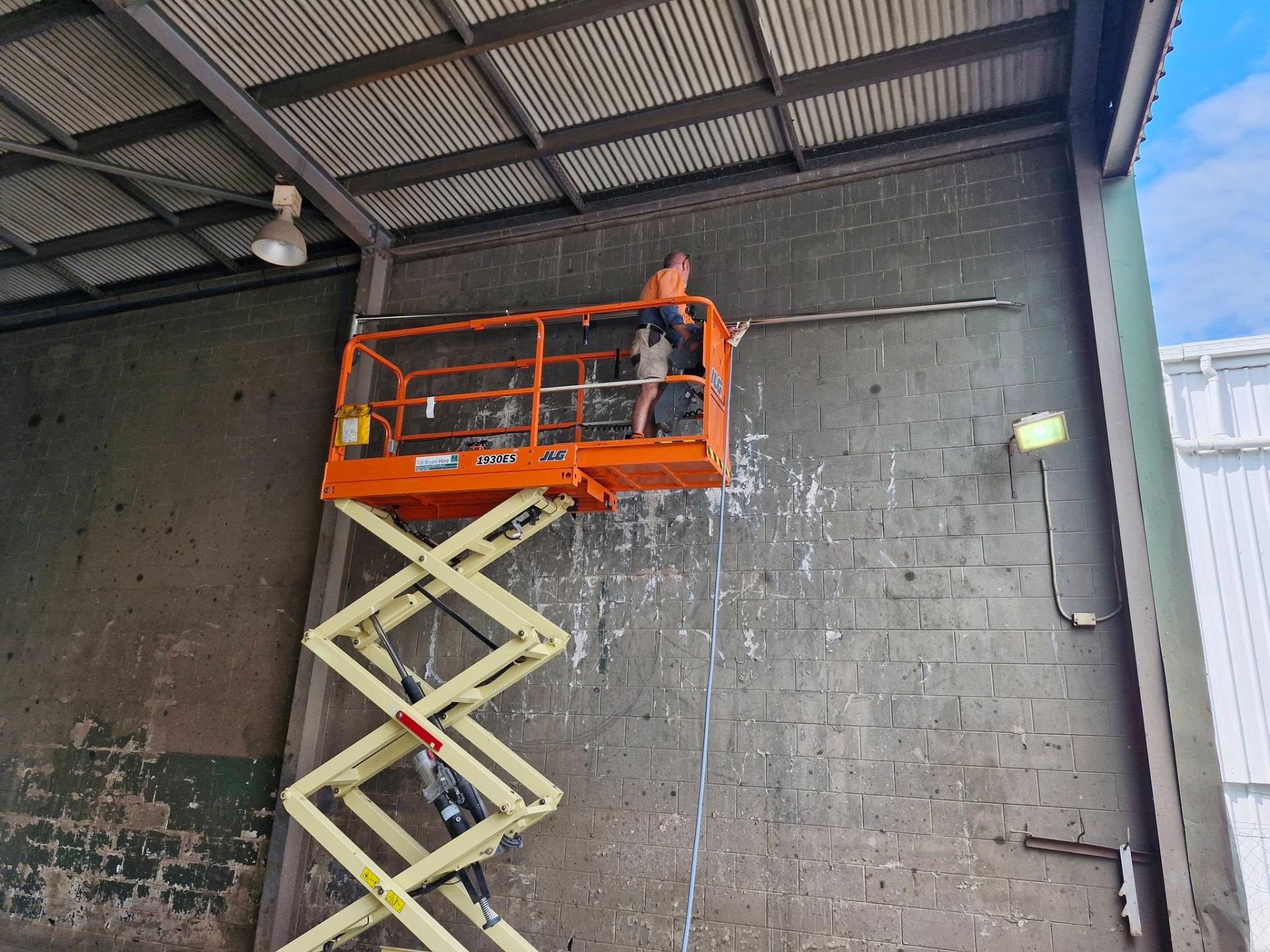 Pressure washing high warehouse walls from a scissor lift